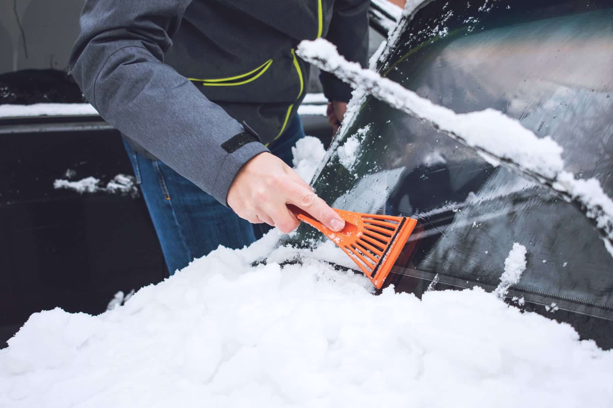 man cleaning car from snow and ice with brush and       utc